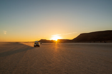 An all-terrain vehicle driving through the desert at sunset