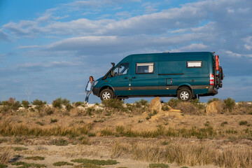 Obraz na płótnie Canvas Woman leaning on a 4x4 camper van in a desert landscape