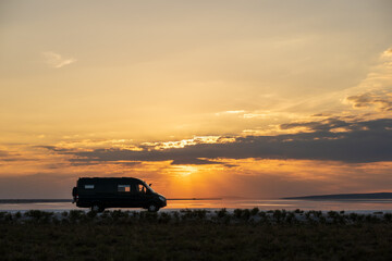 Fototapeta na wymiar Backlighting silhouette of a 4x4 camper van in a desert landscape at sunset