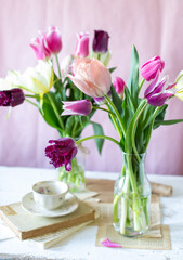 Obraz na płótnie Canvas Mazzi di tulipani dalle sfumature del rosa su bottiglie di vetro sopra un tavolo di legno 