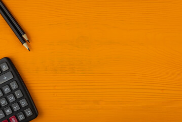 Black pencil and calculator on a yellow, wooden background (copy space).