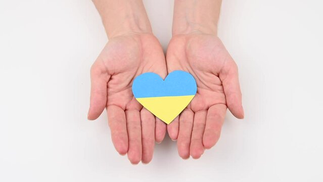 Woman opens her palms with a heart with the flag of Ukraine. 