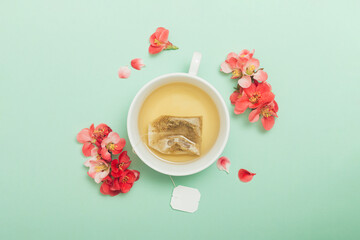White ceramic cup with tea and red flowers on a pastel green background. Flower tea concept. Tea bag. Top view