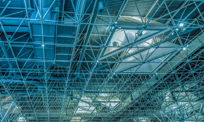 Steel roof structure seen from interior with exposed structural steel tubing, ventilation ducts and industrial light fixtures, nobody
