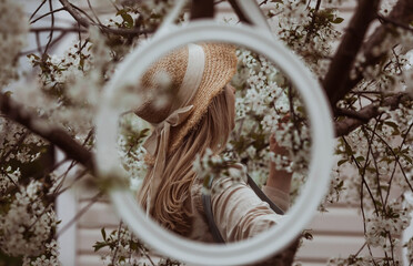 Vintage. Reflection in the mirror. A beautiful, young woman in retro clothes and a straw hat in a blooming cherry orchard. Visual for content.