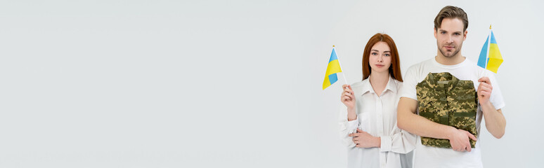 Young couple holding military uniform and ukrainian flags isolated on white, banner.