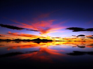 Fototapeta na wymiar Dramatic sunset sky over mysterious lake in desert Salar de Uyuni. Mystical twilight over dark water. Impressive sundown in Andes. Fiery heaven clouds reflection in water.