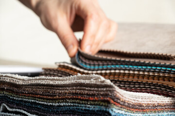 A catalog of different colors of fabrics in the hands of a girl for the choice of a client for upholstery, examples of multi-colored fabrics as a background, fabrics
