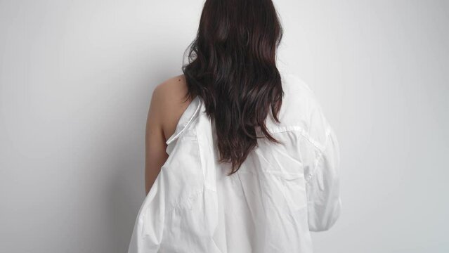 A rear view of a woman taking off a white shirt from herself and her body becomes naked. Naked woman