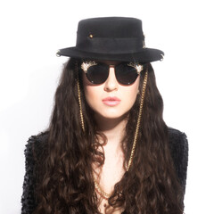 Beauty, fashion and make-up concept. Beautiful woman with long dark curly hair, black hat, shiny suit and sunglasses with jewelery studio portrait. Bright and soft image with star shining filter