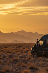 Rugged reliefs of the mountains in the Iranian desert at sunset with a 4x4 camper van on the side