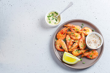 Shrimps cooked with spices lie on a plate with lemon, salt, herbs and sauce on a gray background. copy space