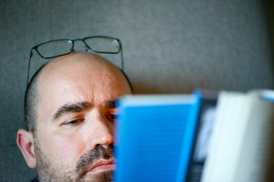 hobre leyendo un libro azul con los lentes en la cabeza, luz natural, libro desenfocado, fondo gris
