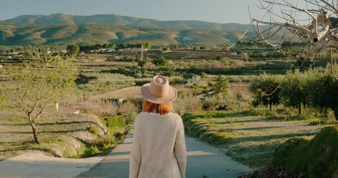 Back view of woman with hat walking along the road on background the mountains