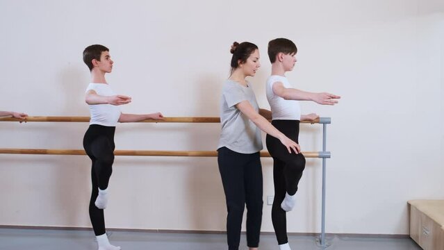 Ballet gymnastics class: teacher helps students to hold the dance position and perform exercise. Junior Dance School for children and teenagers, classical dances lesson. Choreography education