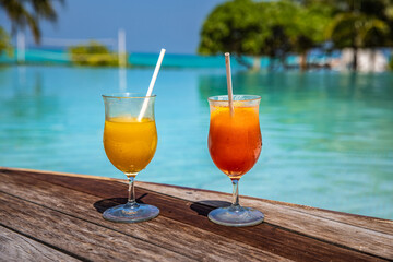 Two cocktails on luxury tropical beach resort. Couple vacation, travel holiday, summer island poolside with drink, leisure lifestyle at beach bar on wooden floor. Outdoor swimming pool and beverages