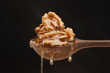 Transparent honey pouring down from wooden spoon with walnuts on a black background. Shallow depth...