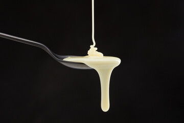 Sweetened condensed milk pouring down from spoon on a black background. Coconut milk with droplet....
