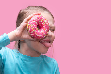 A cute funny girl in a blue t-shirt holds a bright pink donut near her eye and shows you her tongue...