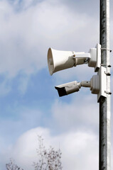 Loudspeaker and video camera on a wooden pole against the blue sky. Vertical photography.
