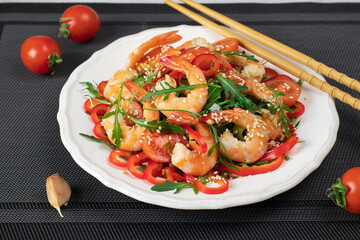 Salad with shrimps, arugula, cherry tomatoes, sweet peppers and sesame seeds on white plate