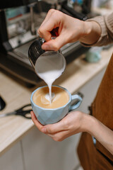 Fototapeta na wymiar The hand of a barista girl pouring milk into coffee. Cafe, breakfast, morning