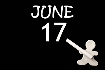 A small white plasticine man writing the date 17 June on a black board. Business concept. Education concept.
