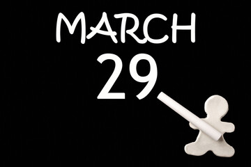 A small white plasticine man writing the date 29 March on a black board. Business concept. Education concept.