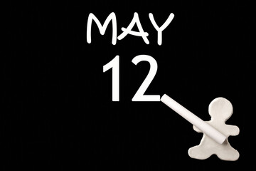 A small white plasticine man writing the date 12 May on a black board. Business concept. Education concept.