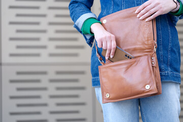 Woman putting mobile phone in brown leather handbag closeup