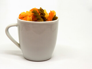 Studio shot of a heap of colorful raw fusilli pasta on a modern ceramic cup against neutral background