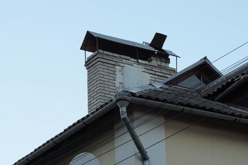 one gray brick chimney on a tiled roof with a metal drainpipe on a brown wall of a house outside