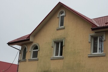 brown attic of a concrete private house with windows under a red tiled roof against a gray sky
