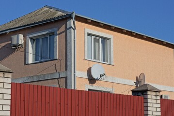 private brown house with white windows behind a red metal fence against a blue sky