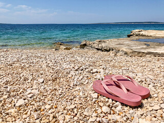 Fototapeta na wymiar Rosa Flip Flops am Kieselstrand von Mandre, Insel Pag, Kroatien