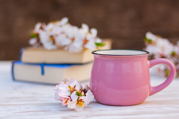 close-up pink cup and a blossoming spring twig of an almond tree on a table next to books. spring still life