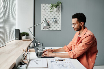 Serious busy young black marketing specialist in eyeglasses working with laptop in minimalistic...
