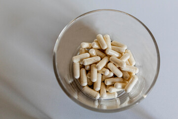 Lots of brown and white oblong capsules in a glass close-up on a light background top view, high quality photo