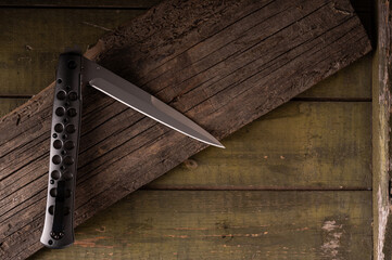 Folding knife with lightweight handle. Knife handle with holes. Knife on a wooden background. Sharp big knife.
