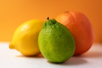 Group of citrus, lime, lemon, and orange, against an orange background.