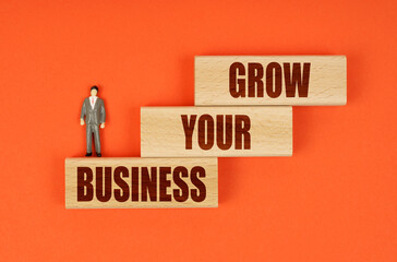 On wooden blocks with the inscription - GROW YOUR BUSINESS, there is a miniature figure of a...