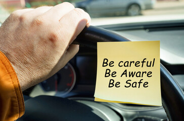 A man holds on to the steering wheel, next to a sticker with the inscription - Be careful. Be...