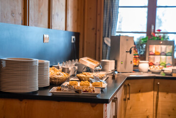 Various baked food by stack of plates on counter. Delicious breakfast displayed at dining hall. Concept is of catering in luxurious ski resort.