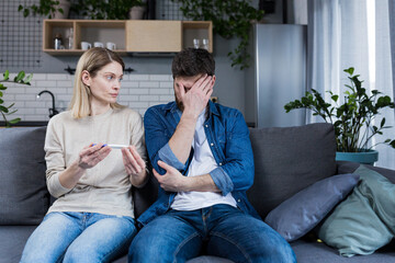 Obraz premium Frustrated man and woman sitting on the couch at home, received a negative pregnancy test