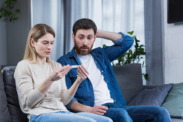 Sad man and woman sitting on the couch, disappointed with a negative pregnancy test
