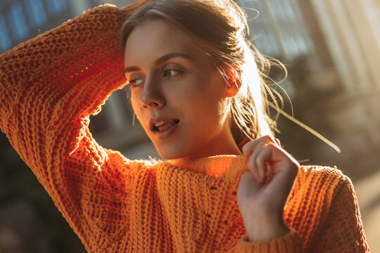 Beautiful young blonde woman posing on the camera outdoor. Close up portrait of female model in orange warm sweater. The girl looking sideway and open her mouth