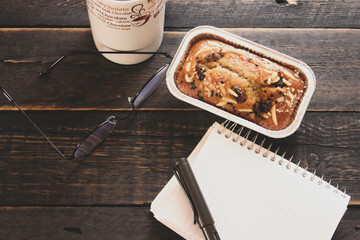 Banana Cake on a black wooden table With note book, glasses, and coffee mugs.