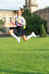 Happy energetic girl child in uniform back to school jumping for joy, September 1