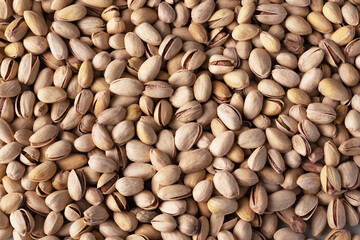 Close-up view of a dense collection of raw pistachio nuts with varying shades of brown.