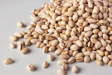 Pile of shelled pistachios on a light background, some scattered around the main heap.